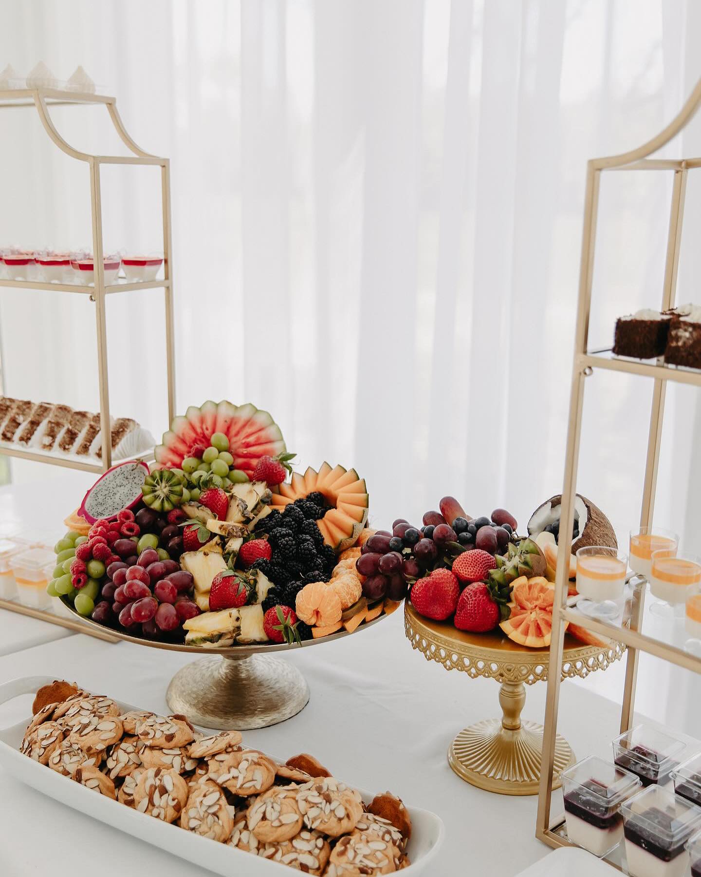 Fruits, cookies, and pastries on a white table cloth.