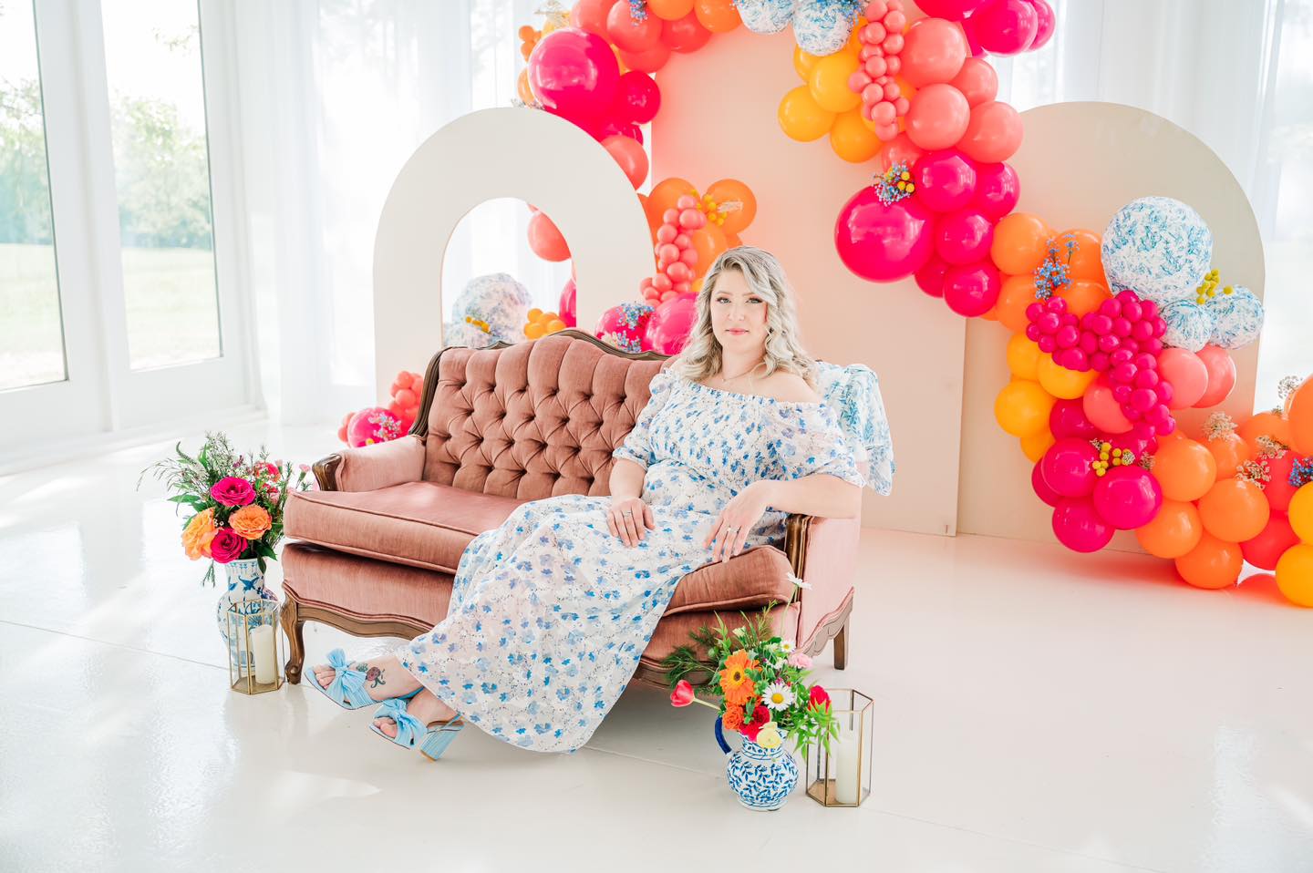 woman in pink chair in front of pink and orange balloon arch