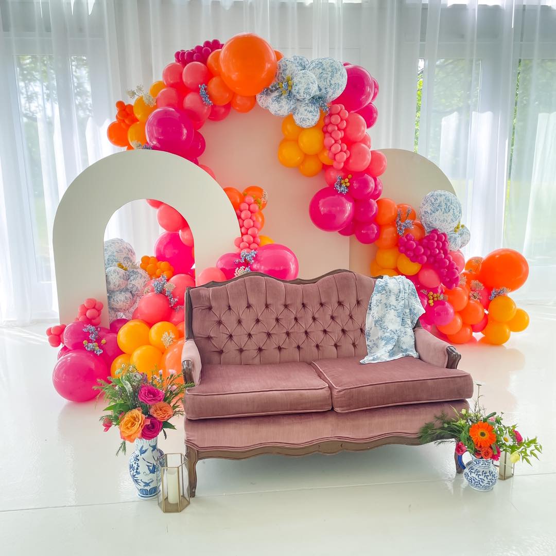 pink couch in front of orange and pink balloon arch