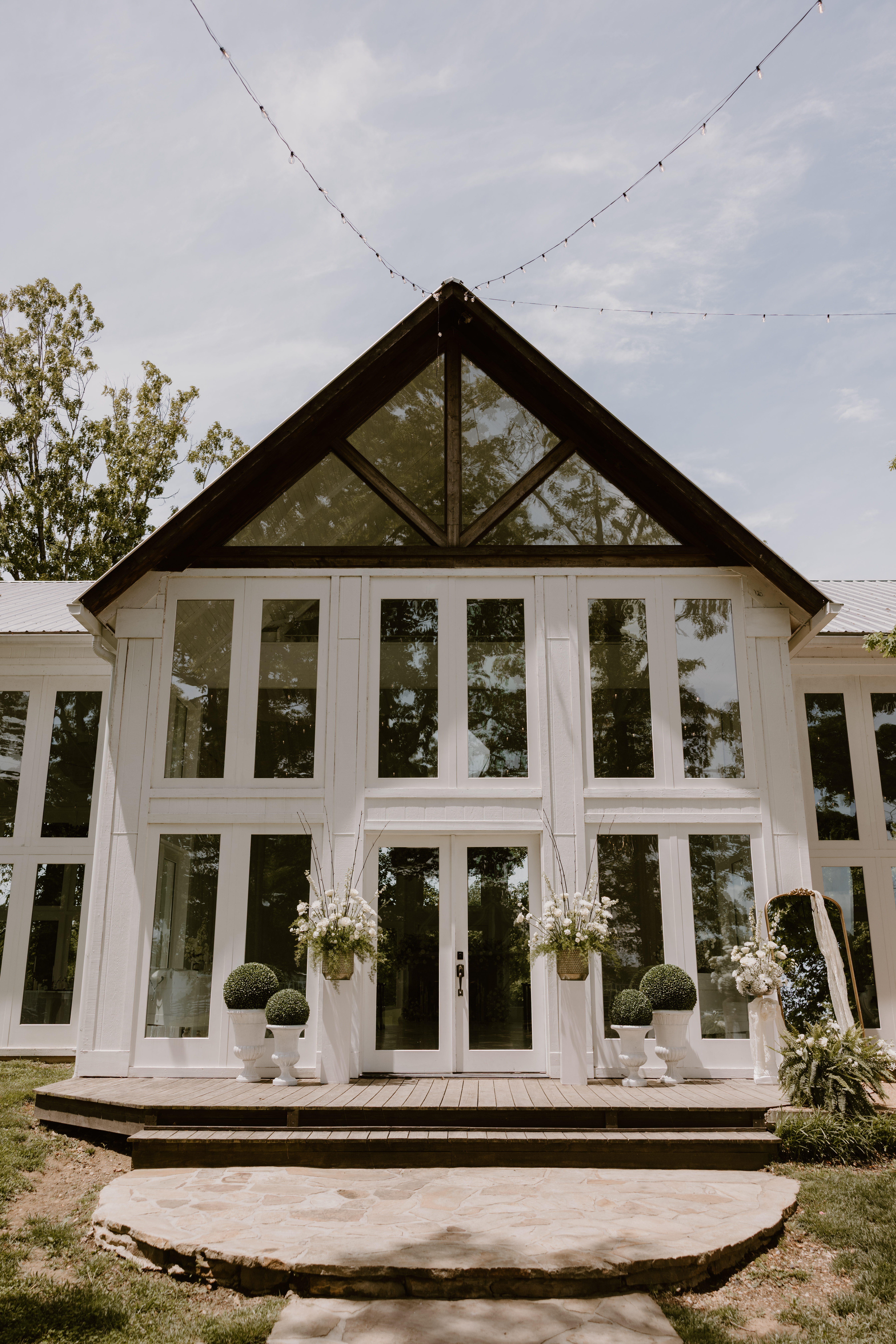 Front of venue with white windows, doors, and flowers hanging up.