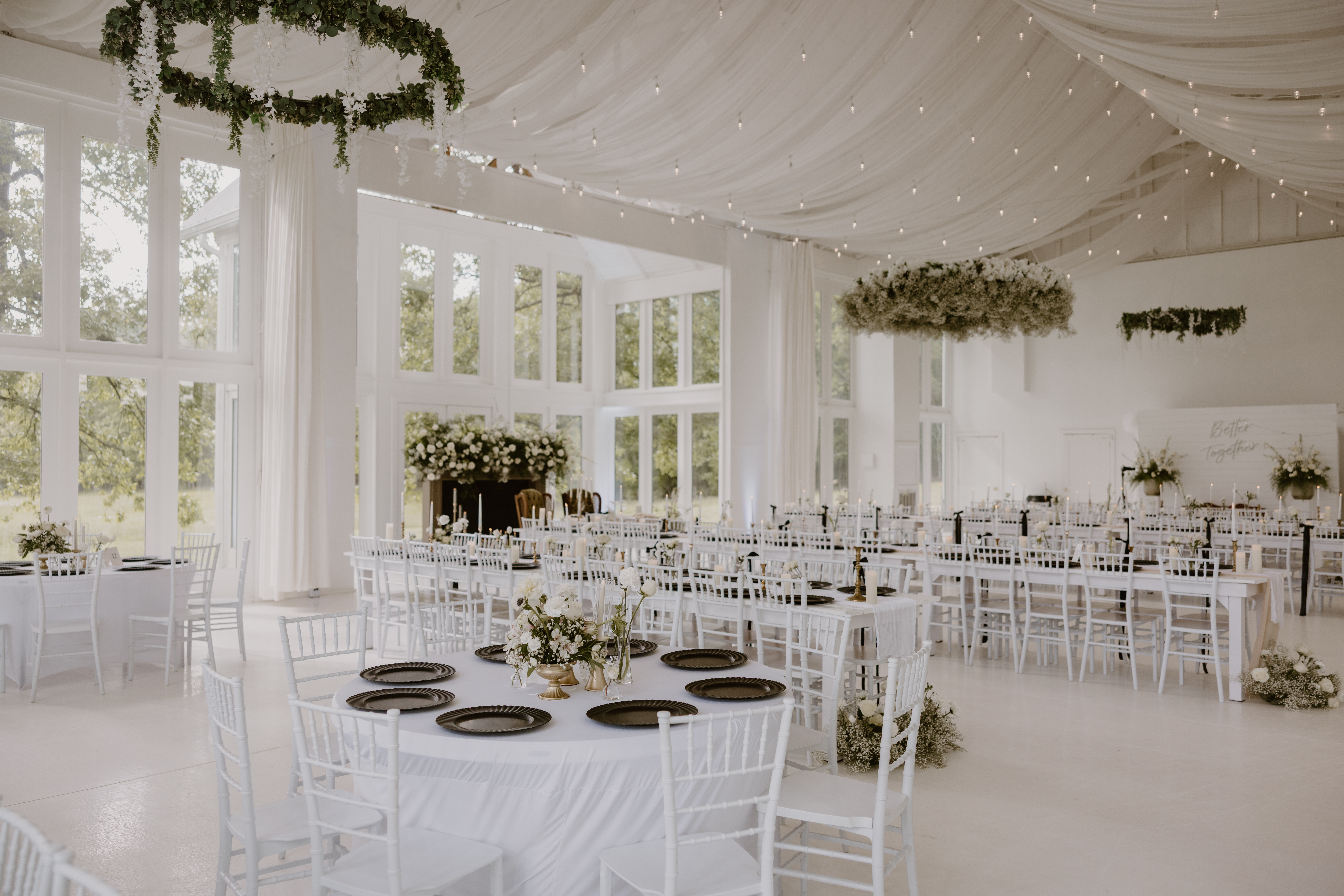 reception set up with greenery, white tables and chairs, and lights.